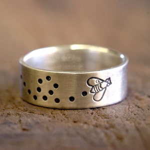 Può includere: Un anello d'argento con un design a forma di ape e una fila di punti attorno alla fascia.
