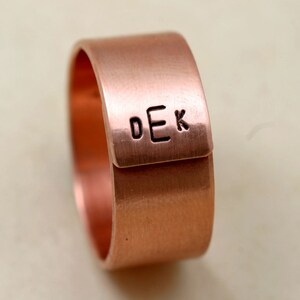 May include: A copper ring with a flat band and a personalized inscription that reads "DEK".