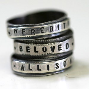 May include: Stack of three silver rings with engraved words "MEREDIT", "BELOVED", and "ALLISON".