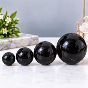 May include: A set of four polished black stone spheres arranged in a row from smallest to largest. Each sphere has a smooth, reflective surface with subtle natural veining and deep dark tones, showcasing a spherical shape and glossy finish.
