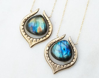 May include: Two gold necklaces featuring labradorite gemstone pendants. Each pendant is a teardrop shape with a smooth, polished stone set in a gold frame.
