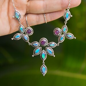 May include: A silver necklace with a floral design featuring opal and ruby gemstones. The necklace has a pendant with a single opal gemstone.