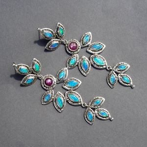 以下が含まれることがあります： 青いオパールとピンクの宝石のアクセントが付いたシルバーのイヤリングのペア。イヤリングは葉のクラスターの形をしています。