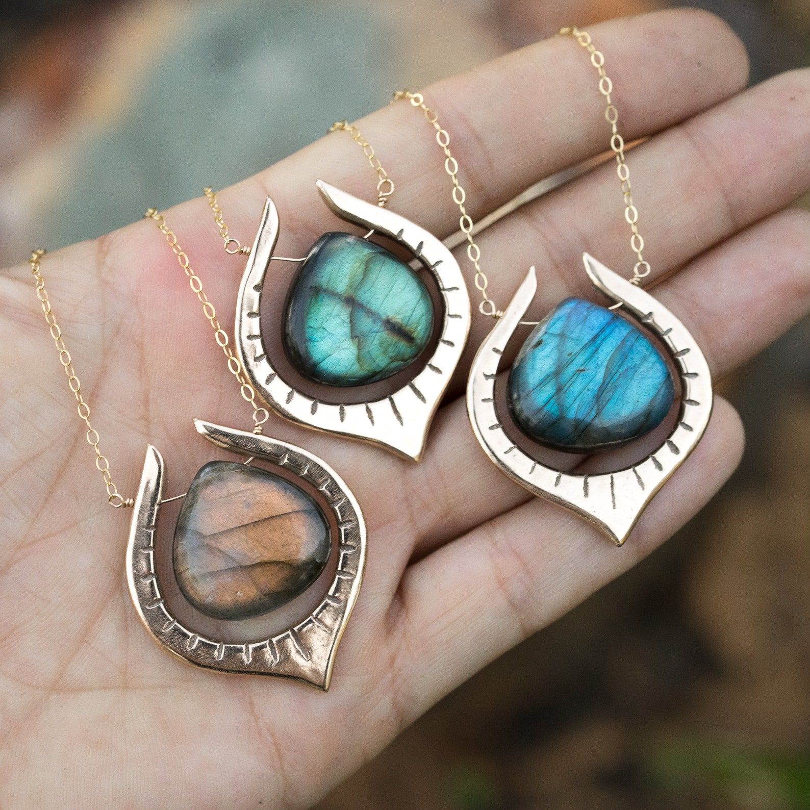 Labradorite teardrop pendants in bronze settings with glowing blue and green flashes, held in a hand.
