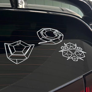 May include: A white car with a black rear spoiler and a black rear window. There are three white geometric stickers on the rear window.