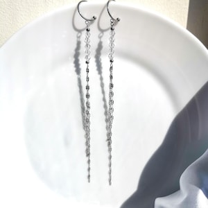 Puede incluir: Un par de pendientes de aro de plata con una cadena larga y colgante de pequeñas cuentas de plata y un acento de cuentas de cristal.