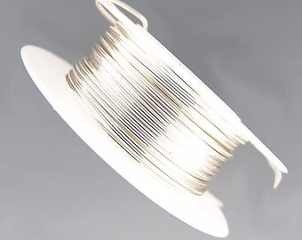 Peut inclure: Gros plan sur une bobine de fil argenté enroulée sur un support en carton blanc. Le fil métallique est fin et brillant. L'image est prise sur un fond gris clair. Le fil est bien enroulé, révélant sa texture et sa couleur argentée.