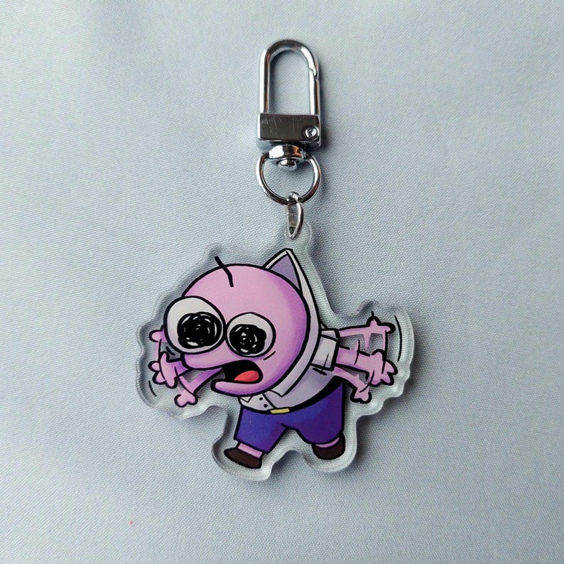 Puede incluir: Un llavero de acr&iacute;lico transparente con un personaje de dibujos animados rosa con ojos grandes y una expresi&oacute;n de sorpresa. El personaje lleva una camisa blanca y pantalones azules. El llavero tiene un anillo de metal plateado.