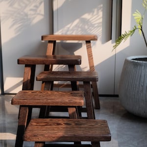 May include: Five wooden stools stacked on top of each other. The stools are made of dark brown wood and have a simple, rustic design.