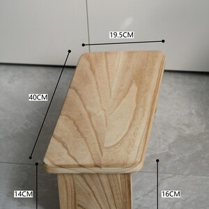 May include: A light-colored wooden step stool with the text "ZENWOOD LIVING" at the top. The stool is 15.7 inches tall, 15.7 inches wide, and 7.7 inches deep. The wood grain is visible on the surface.