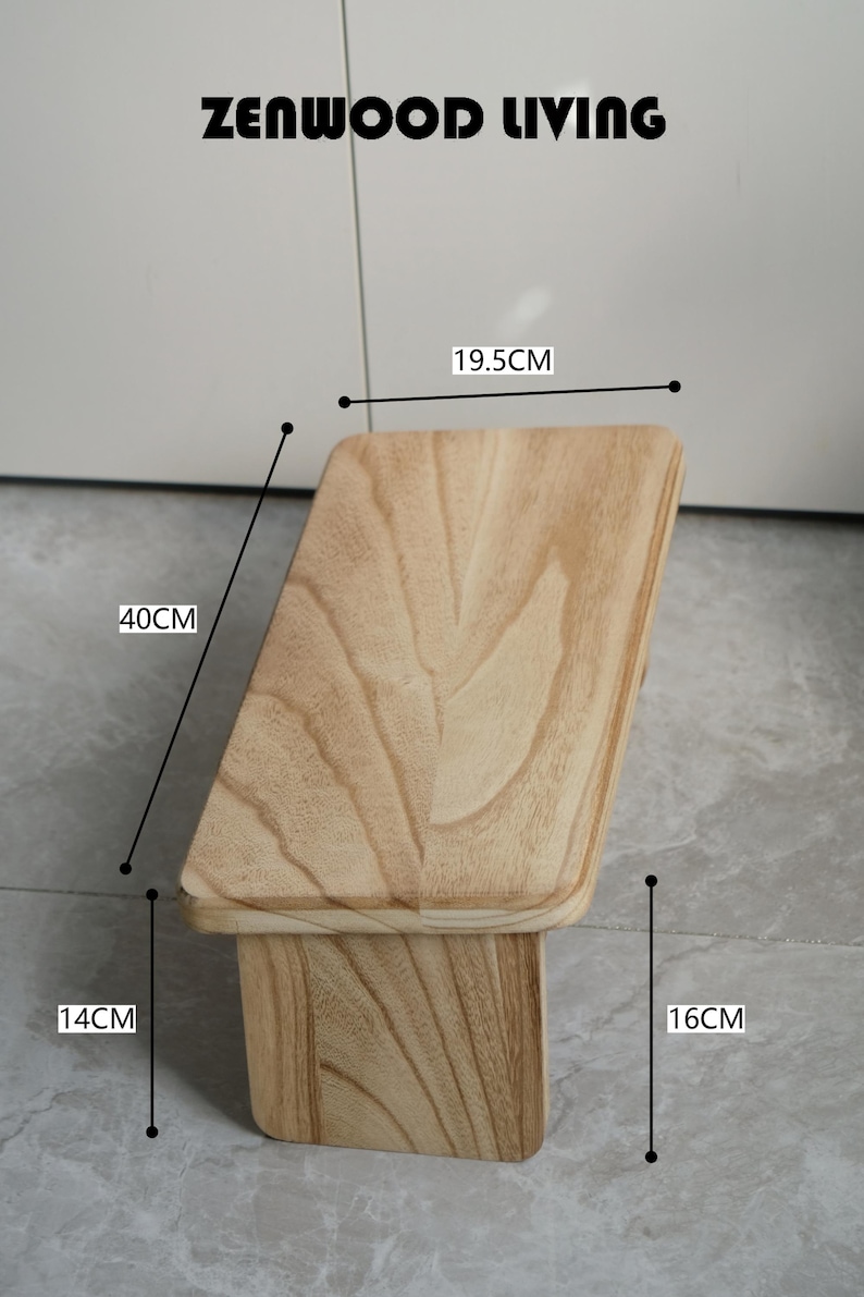 May include: A light-colored wooden step stool with the text "ZENWOOD LIVING" at the top. The stool is 15.7 inches tall, 15.7 inches wide, and 7.7 inches deep. The wood grain is visible on the surface.