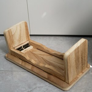 May include: A wooden desk organizer with a natural finish. The organizer has a rectangular base with two upright sides and a central section with a hinged lid. The wood grain is visible throughout the design.