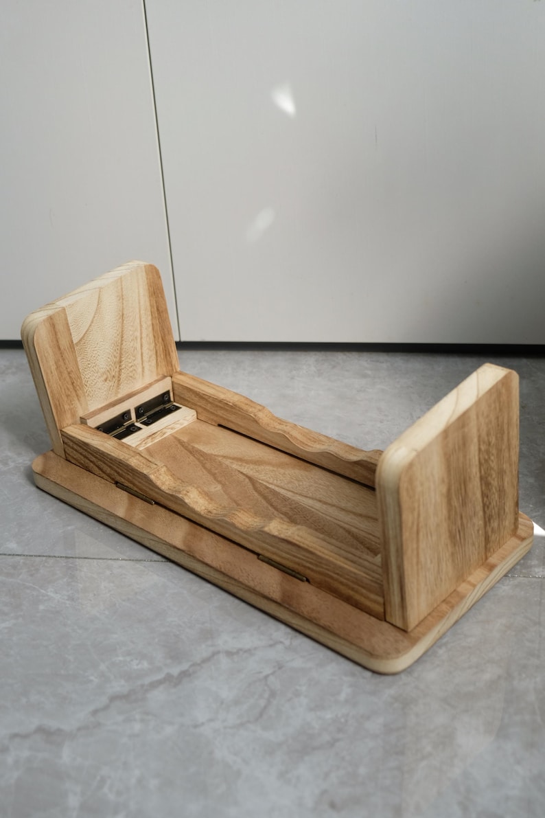 May include: A wooden desk organizer with a natural finish. The organizer has a rectangular base with two upright sides and a central section with a hinged lid. The wood grain is visible throughout the design.