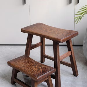 May include: Two wooden stools, one stacked on top of the other. The stools are made of dark brown wood and have a simple, rustic design.