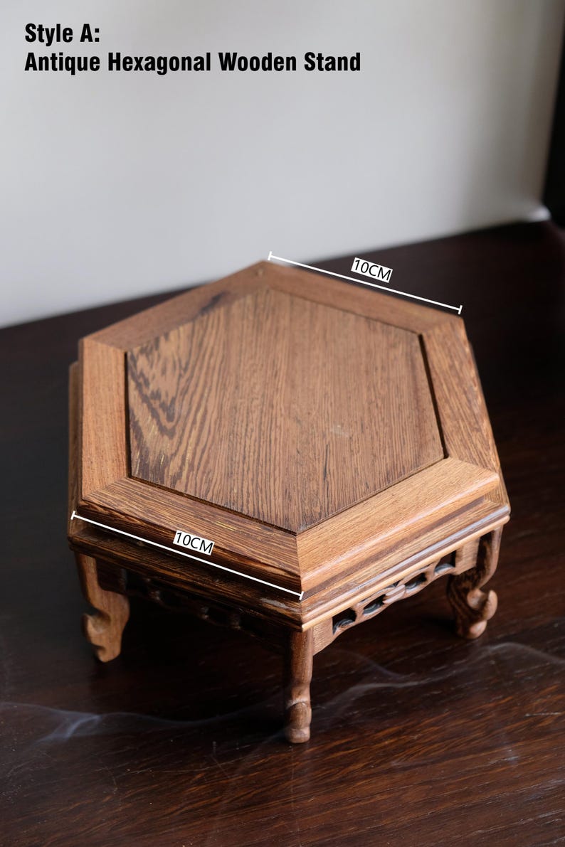 May include: Antique hexagonal wooden stand with a dark brown finish. The stand measures 10 inches in diameter and has intricate carvings on the legs.