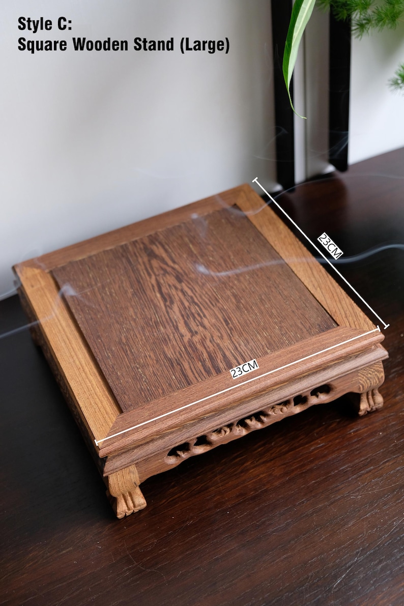 May include: A square wooden stand with a 23-inch by 23-inch top and carved legs. The stand is made of dark wood and has a natural finish.