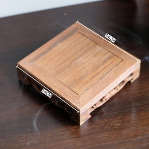 May include: A small, square wooden stand with a natural wood finish. The stand measures 14 inches by 14 inches.