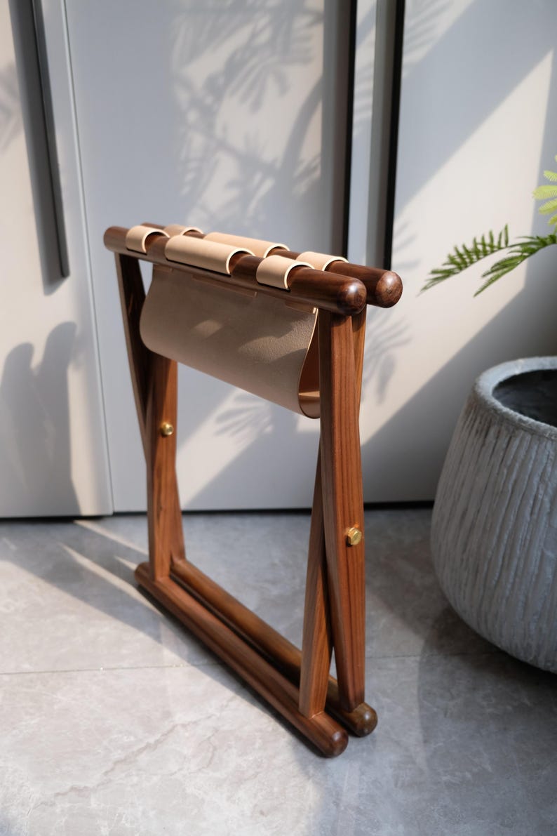 May include: A wooden folding stool with a light brown leather seat. The stool is made of dark brown wood and has a brass accent.