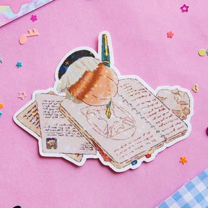 May include: A sticker featuring a cartoon character with brown hair wearing a blue hat and glasses, sitting at a desk with a pen and several open books. The sticker has a glittery finish.