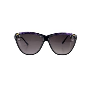 May include: Black cat-eye sunglasses with gradient lenses. The frames have a purple textured design on the top and small gold accents. A fashionable accessory for eye protection.