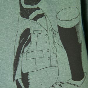 May include: A green t-shirt with a black and white illustration of a penguin wearing a vest and holding a glass of beer.