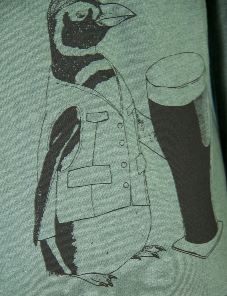 May include: A green t-shirt with a black and white illustration of a penguin wearing a vest and holding a glass of beer.