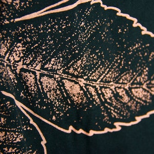 May include: A dark green fabric with a light pink leaf design. The leaf is detailed with veins and a textured surface.