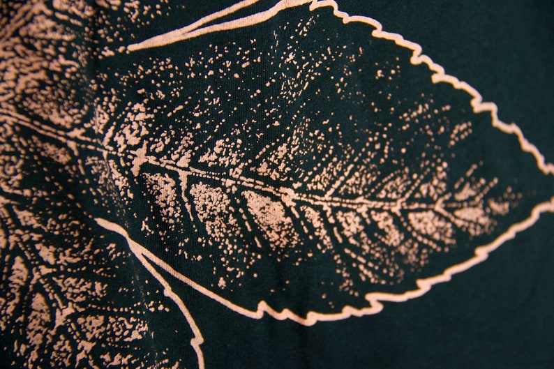 May include: A dark green fabric with a light pink leaf design. The leaf is detailed with veins and a textured surface.