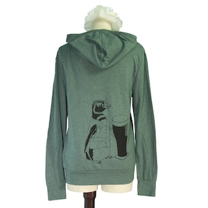 May include: A green hooded sweatshirt with a penguin graphic holding a glass of beer. The penguin is wearing a jacket and has a black and white pattern.
