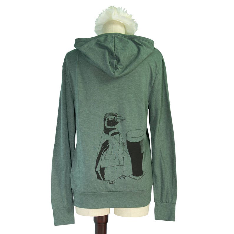 May include: A green hooded sweatshirt with a penguin graphic holding a glass of beer. The penguin is wearing a jacket and has a black and white pattern.