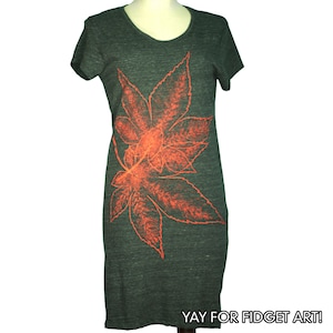 May include: A dark gray t-shirt dress with a large orange leaf print on the front. The text "YAY FOR FIDGET ART!" is printed on the bottom of the dress.