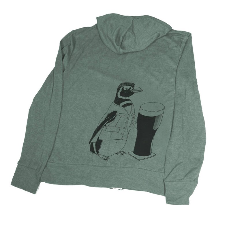 May include: A green hooded sweatshirt with a black and white illustration of a penguin wearing a suit and holding a glass of beer.