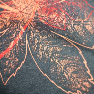 May include: Close-up of a dark gray fabric with a red and orange leaf design printed on it. The leaf design is detailed and intricate.