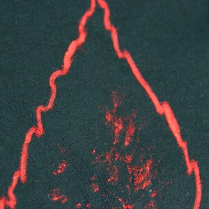 May include: A close-up of a black fabric with a red outline of a flame shape. The flame shape is slightly faded and has a rough texture.