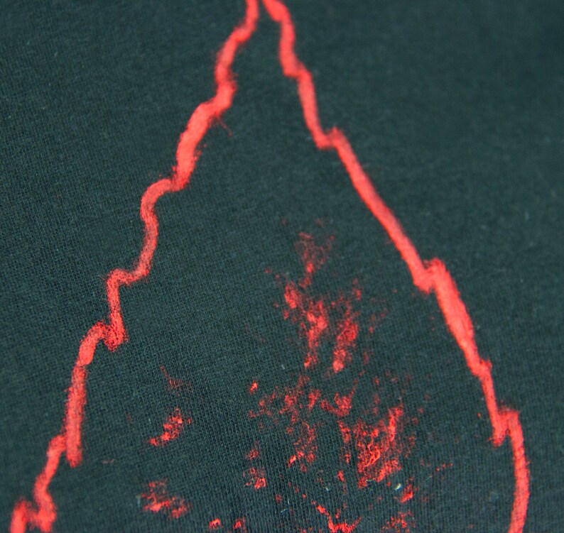 May include: A close-up of a black fabric with a red outline of a flame shape. The flame shape is slightly faded and has a rough texture.