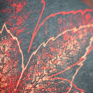 May include: Close-up of a dark gray fabric with a red and orange leaf design. The design is created with a splatter technique, giving it a textured look.
