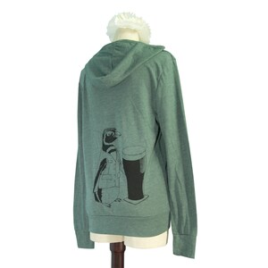 May include: A green hooded sweatshirt with a graphic of a penguin holding a glass of beer. The penguin is wearing a jacket and has a black and white pattern.