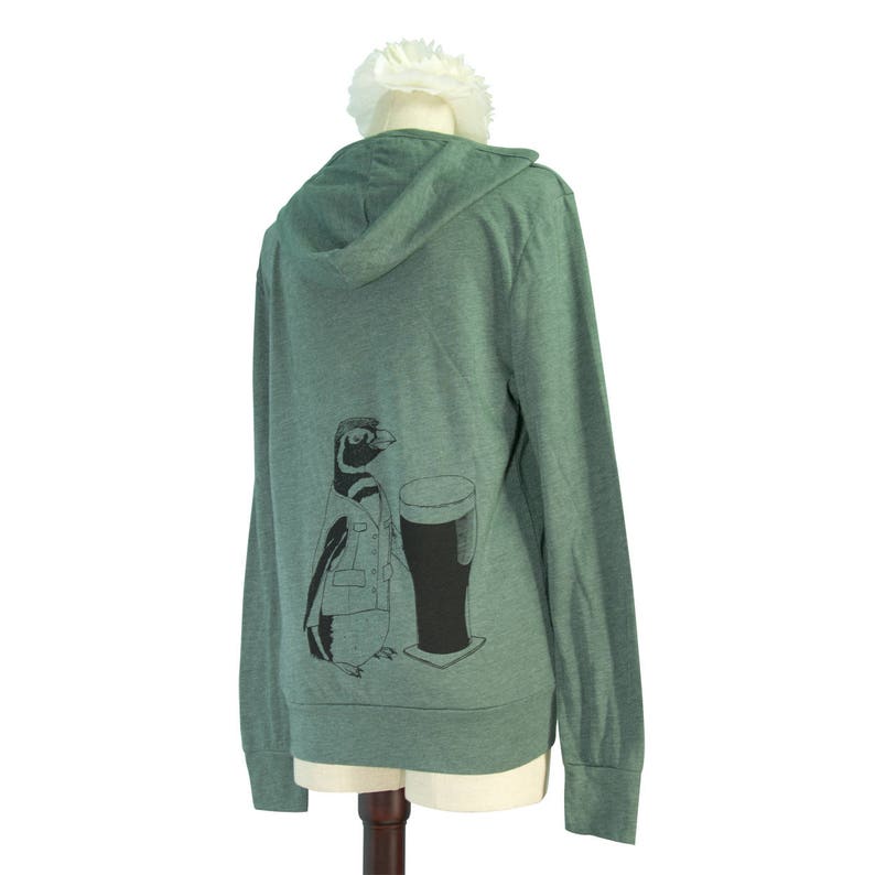 May include: A green hooded sweatshirt with a graphic of a penguin holding a glass of beer. The penguin is wearing a jacket and has a black and white pattern.