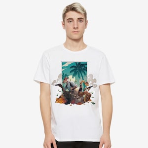 May include: White t-shirt featuring a colorful illustration of a scene with palm trees, a full moon, and figures holding guns. The graphic has a cartoonish style with a tropical theme.
