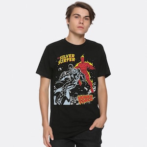 May include: Black t-shirt with a comic book illustration of The Silver Surfer and Human Torch. The design includes the text "The Silver Surfer" in yellow and "Human Torch" in white, with the characters in silver and red.