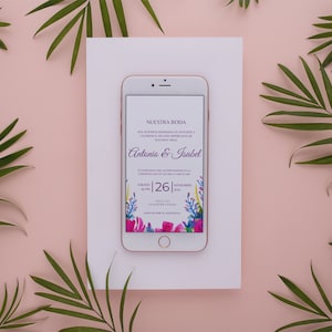 May include: A smartphone displaying a wedding invitation with a floral design. The invitation reads "Nuestra Boda" and features the names "Antonio & Isabel" and the date "Sabado 26". The phone is on a white background with green palm leaves.