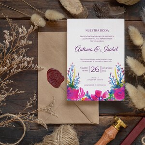 May include: A wedding invitation with a watercolor floral design in shades of pink, blue, and green. The invitation reads "Nuestra Boda" and includes the names Antonio & Isabel, the date Saturday, November 26, 2014, and the time 09 PM. The invitation is on a brown wooden surface with dried flowers and a wax seal.