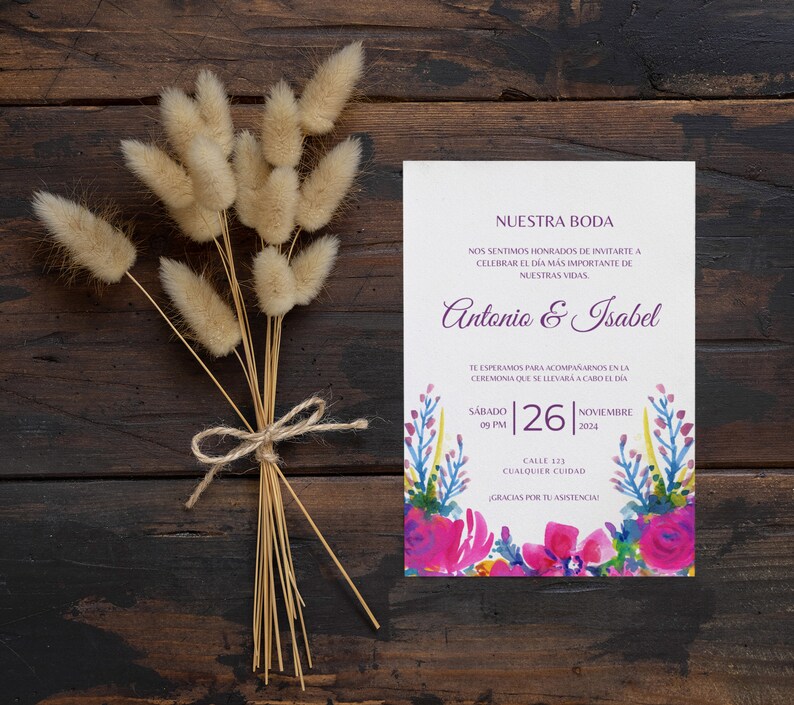 May include: A wedding invitation with a watercolor floral design in shades of pink, purple, blue, and yellow. The invitation reads "Nuestra Boda" and includes the names Antonio & Isabel, the date Saturday, November 26, 2024, and the time 09 PM. The invitation also includes the address Calle 123, Cualquier Ciudad.