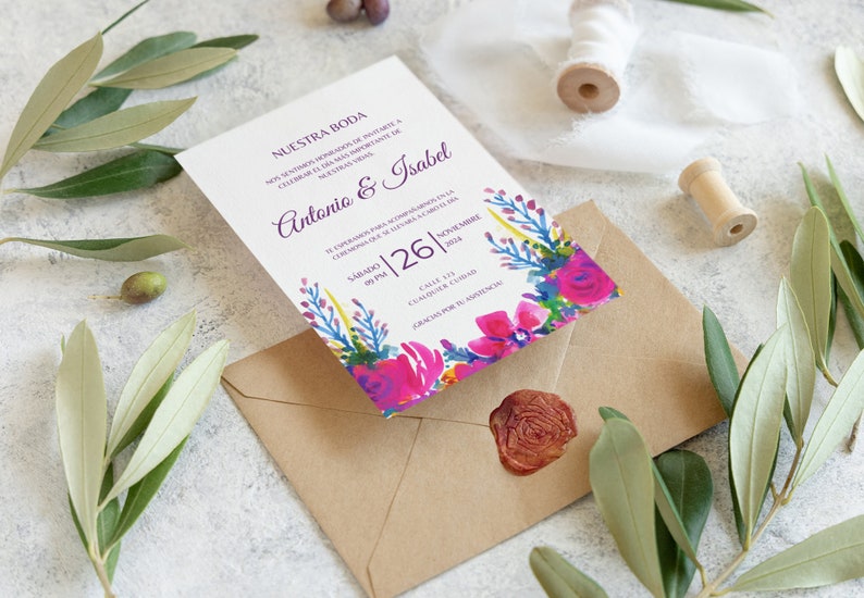 May include: A white wedding invitation with a floral design in shades of pink, purple, blue, and green. The invitation reads "Nuestra Boda" and includes the names "Antonio & Isabel" and the date "Sabado 26 | Noviembre 2024".