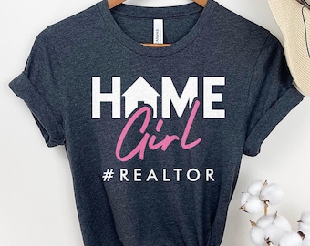 May include: A dark gray t-shirt with white text that reads "HOME Girl #REALTOR" in a pink and white font.