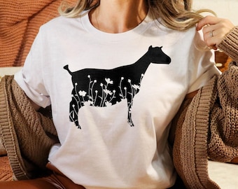 Peut inclure: T-shirt blanc avec une silhouette noire de chèvre avec des fleurs en arrière-plan.