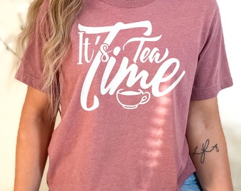 May include: A mauve cropped t-shirt with the text "It's Tea Time" in white lettering. The text is in a stylized font and includes a small illustration of a teacup.