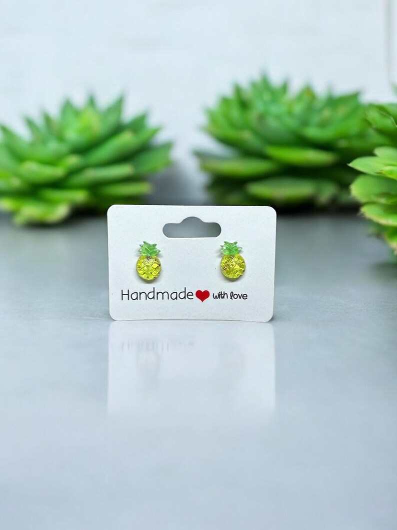 以下が含まれることがあります： 白いカードに「Handmade with love」と書かれた、黄色のパイナップルスタッドイヤリングのペアです。