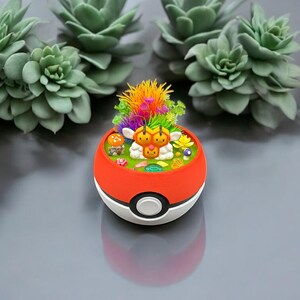 May include: A red and white decorative planter shaped like a Poké Ball, featuring a miniature garden with colorful flowers and a cartoon character. Several green succulent plants are arranged in the background.