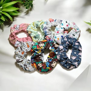 May include: Six colorful scrunchies with various cartoon character prints. The scrunchies are made of fabric and have a gathered, ruffled look.